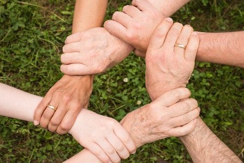 6 Hände von Menschen unterschiedlichen Alters, die im Kreis zusammenhalten